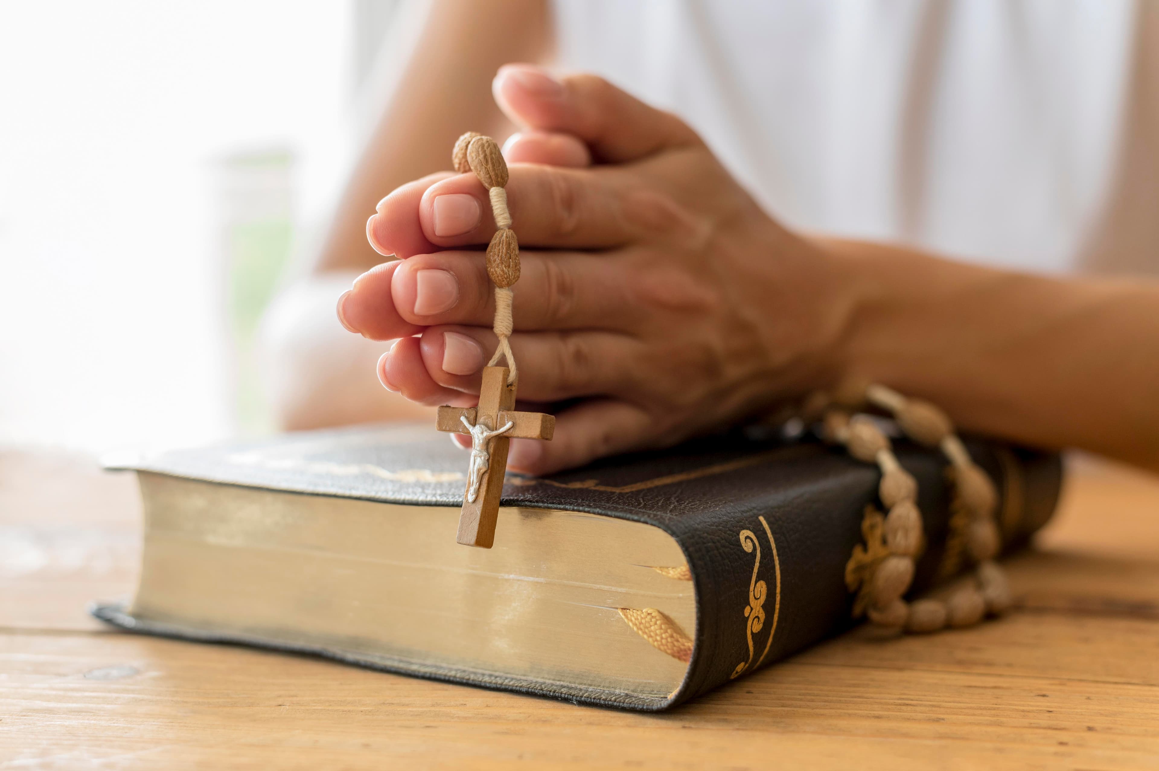 mãos unidas em oração segurando um terço sobre a bíblia sagrada